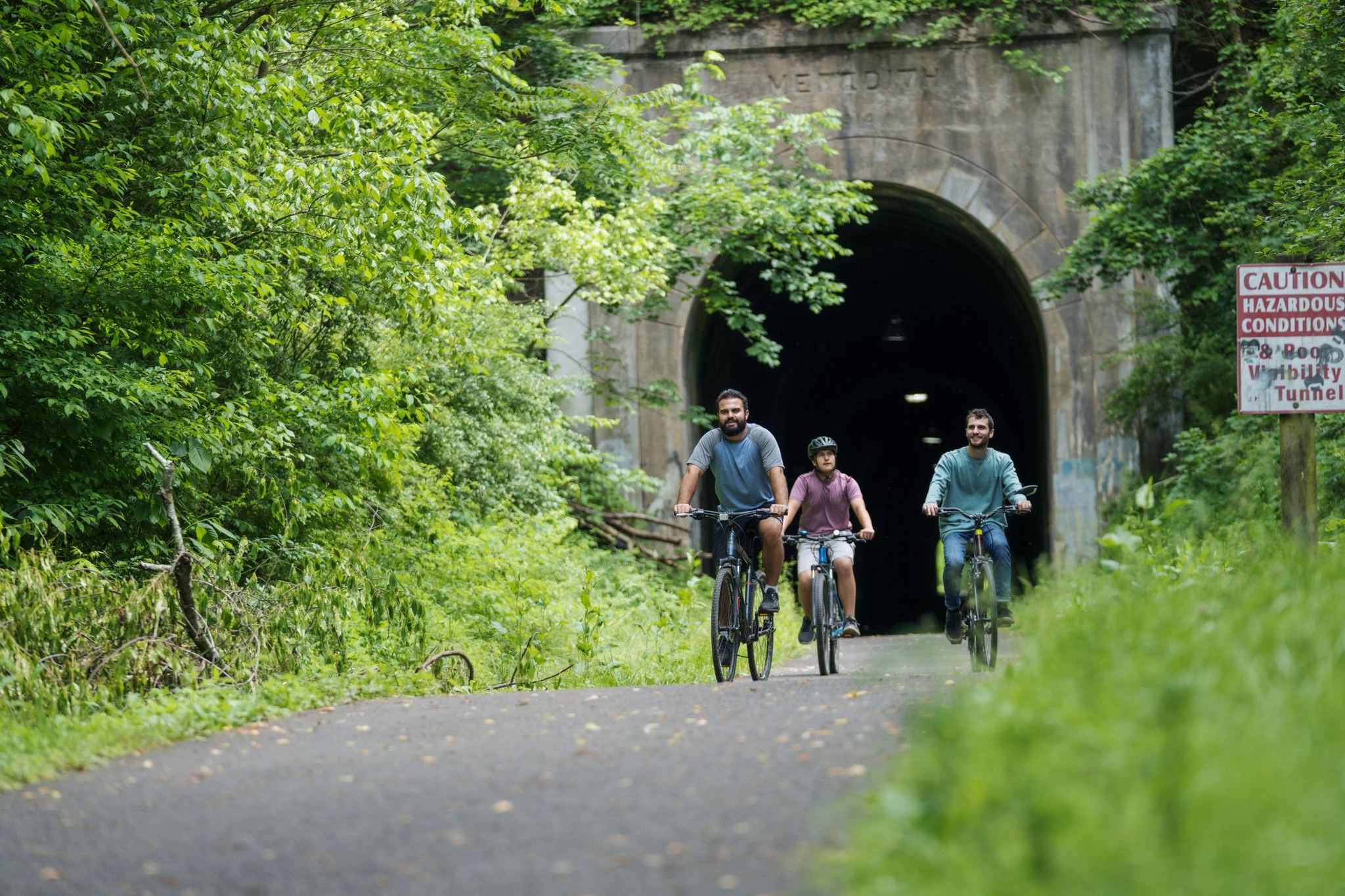 three guys on bicycles coming through a tunnel