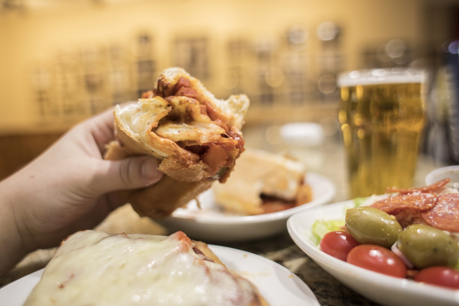 hand holding a hoagie with a glass of beer and a salad in the background