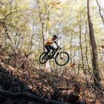 photo of man on mountain bike jumping over a cliff onto ground covered in leaves. River to have a wedding at